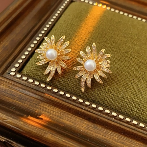 Macro shot of gold floral pearl earrings with shimmering pavé zircon on green velvet