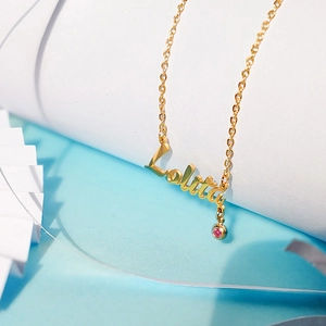 Macro shot of Lolita gold name necklace with a pink birthstone pendant on blue background