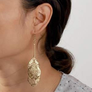 Close-up of golden multi-layer hollow geometric leaf pendant earrings on model
