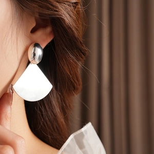 Macro detail of brushed silver-tone fan-shaped earrings worn on a model's ear