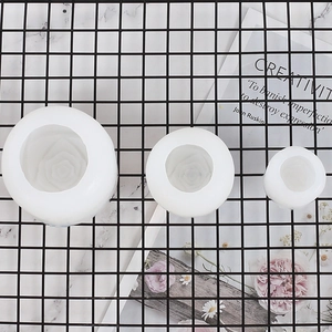 Three sizes of rose-shaped white silicone molds for DIY candles and ice on marble surface