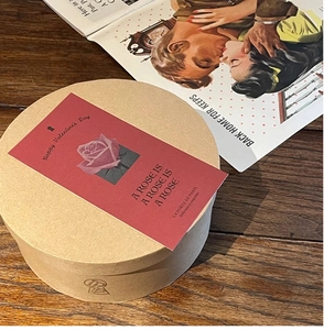 Detail of round kraft paper box with floral Valentine tag on vintage wood surface