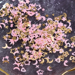 Close-up of pink and golden star, moon, and heart nail art sequins on a glass plate