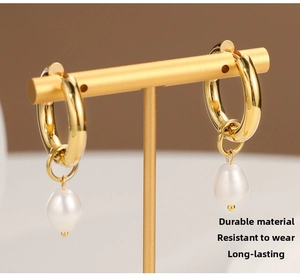 Detailed view of gold plated stainless steel hoop earrings with baroque pearl drops on a stand