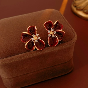 Macro shot of dark red enamel flower earrings with gold accents on brown velvet