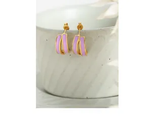 Macro detail of gold-plated double-layer earrings with purple enamel on a ceramic cup