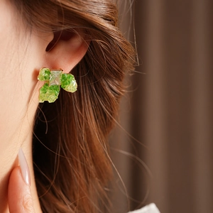 Close-up of green leaf earrings with square clear gemstones on model in gold plating