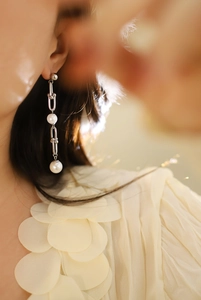 Détail de boucles d'oreilles longues avec perles blanches et maillons en métal argenté