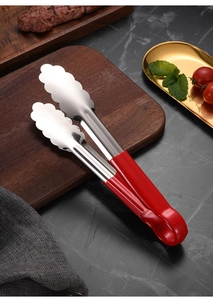 Close-up of stainless steel food tongs with red non-slip handles on a dark wooden board