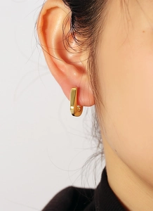 Detailed close-up of a model wearing minimalist golden U-shaped geometric earrings