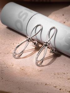 Détail de boucles d'oreilles nœud argentées sur pierre beige avec lumière douce