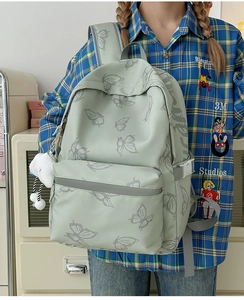 Detail of light green backpack with butterfly print, front pocket and side buckles