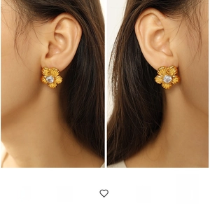 Detailed close-up of golden floral earrings with clear central zircon and textured petals