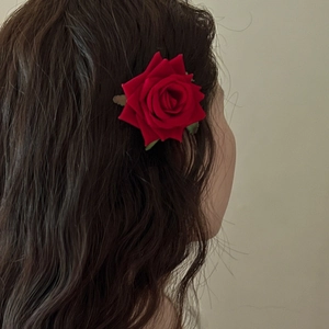 Elegant red velvet rose hair clip with green leaf detail on wavy brown hair
