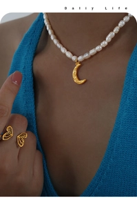 Close-up of a gold moon pendant pearl necklace and butterfly ring on a model