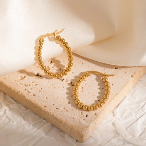 Close-up of 18k gold plated beaded hoop earrings on elegant beige stone backdrop