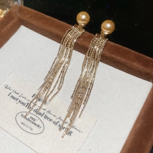 Macro shot of gold long tassel earrings with pearls on a textured white background