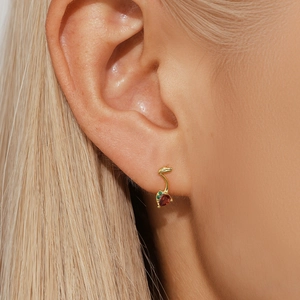 Detail of leaf-shaped gold stud earring with red gemstone on a model's ear