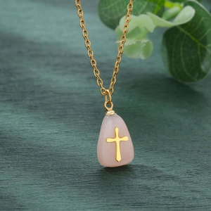 Detailed shot of a pink teardrop stone pendant with gold cross on a green background