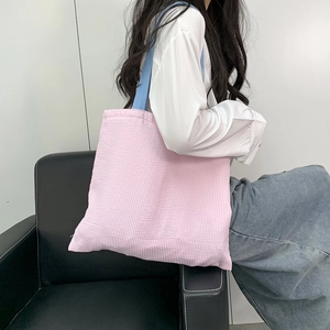Detail of pink and white checkered canvas tote bag with contrast blue handles on shoulder