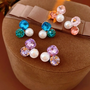 Macro shot of triangle stud earrings with white pearl and colorful crystals on brown velvet