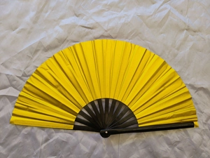 Close-up of a 33cm yellow Kung Fu fan with black bamboo ribs on white fabric
