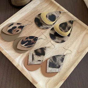 Vintage leopard print and leather teardrop dangle earrings on a wooden display tray