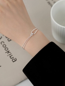 Detail of a minimalist silver knot bracelet on wrist with a double-layered chain design