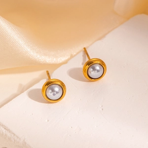 Close-up of minimalist grey pearl earrings with gold bezel on champagne silk fabric
