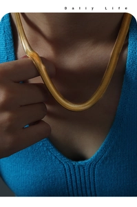 Close-up of a wide gold-plated flat snake chain necklace with detailed wave texture