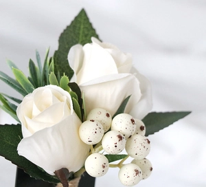 Close-up of elegant wedding boutonniere with white silk roses and green foliage