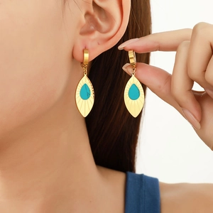 Elegant gold leaf earrings with turquoise center on model in warm studio lighting