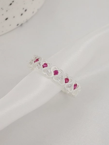 Dettaglio dell'anello a cuore in argento con pietre rosse su sfondo di seta bianca