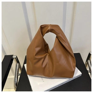 Close-up of caramel brown tote bag with unique knotted handle on a modern chair