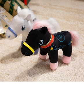 Detail of plush horse toys in black and white with colorful saddles on a cozy rug