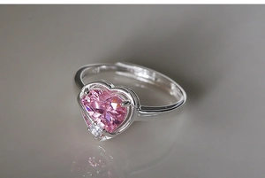 Macro shot of silver heart ring with pink gemstone and small diamond on a reflective surface