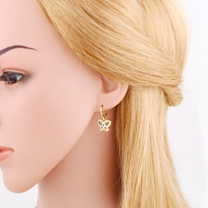 Detail of gold butterfly earring with blue evil eye and sparkling zircons on model
