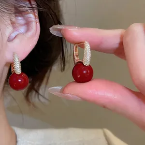 Elegant gold hoop earrings featuring red spherical charms and sparkling micro zircons