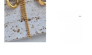 Macro shot of 18k gold chunky link chain with tassel detail on white stone texture