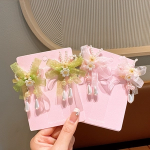 Close-up of handmade floral hair clips with green and pink ribbons and pearl tassels