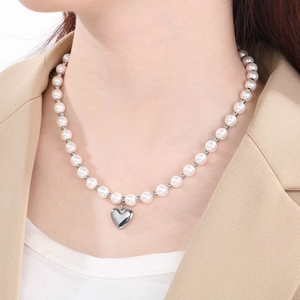 Detail of a white pearl necklace with a silver heart pendant on a professional model