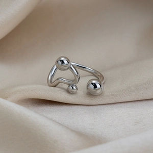 Détail d'une bague ouverte argentée à trois billes sur fond de soie beige