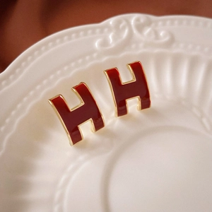 Detailed macro view of H-shaped burgundy enamel studs with premium golden plating