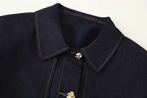 Détail de veste en jean bleu foncé avec surpiqûres jaunes et boutons en métal doré