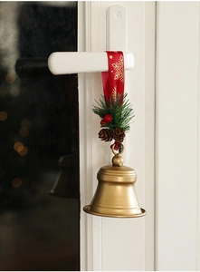 Golden Christmas bell hanging with red snowflake ribbon and pine cone on door handle