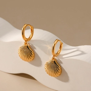 Detailed view of gold scallop shell drop earrings on a white textured display stand