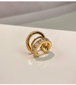 Detail of three-layer gold ear cuff with pearls and zircon stones on a clean background