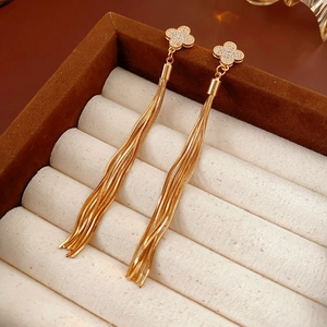 Macro shot of gold four-leaf clover tassel earrings with white zircons in a velvet box