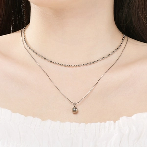 Vue détaillée d'un collier à double épaisseur en acier inoxydable avec pendentif boule.