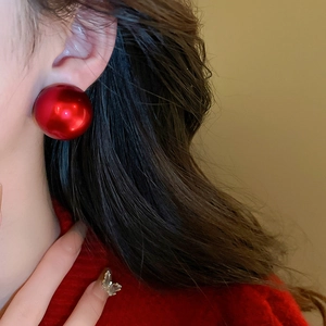 Macro detail of glossy red round stud earrings paired with a silver butterfly ring